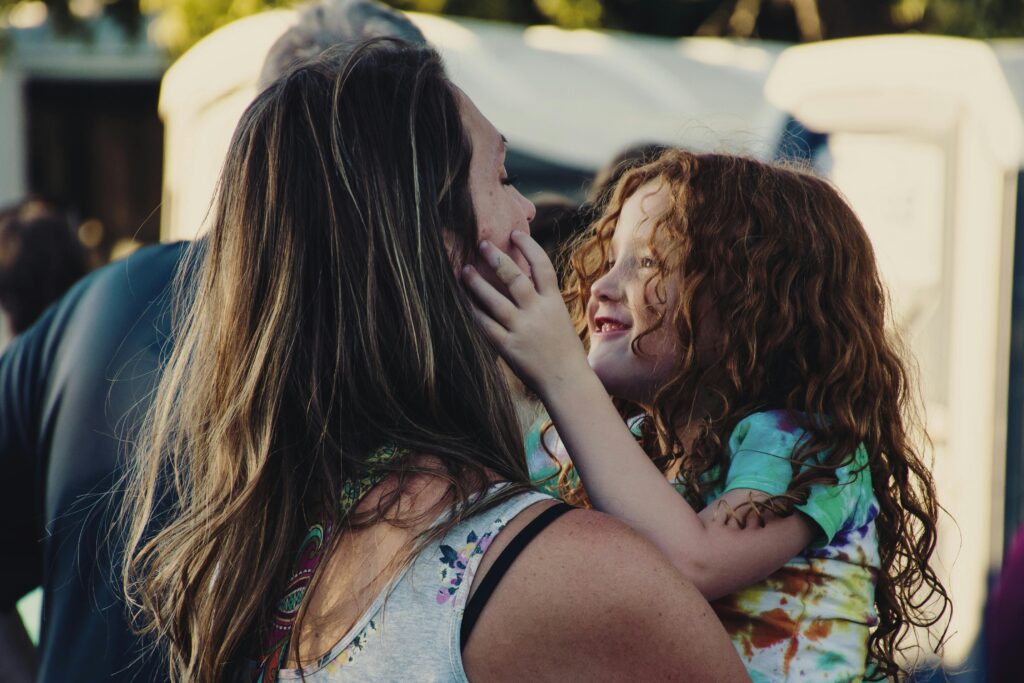 Maman avec son enfant qui sourit dans les bras et qui lui pince gentiment la joue